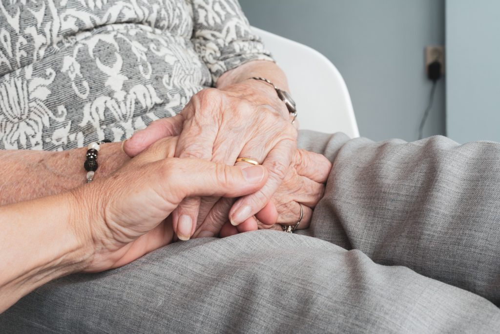 Particolare di un giovane uomo che stringe le mani di una donna anziana con alzheimer con intenzione di comunicare sicurezza. 