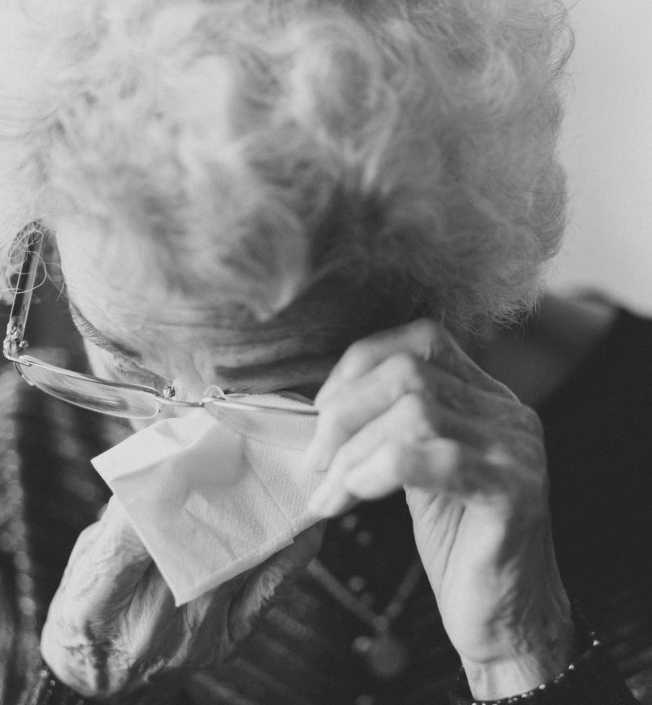 Donna anziana che si asciuga le lacrime agli occhi con un fazzoletto, frustrata dal non riuscire a comunicare efficacemente i suoi bisogni, i suoi sentimenti.
